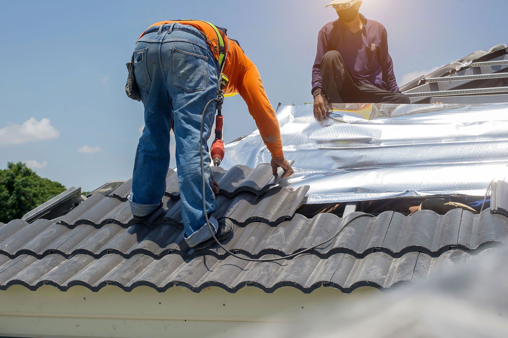 Two construction workers installing roof tiles on a sunny day.