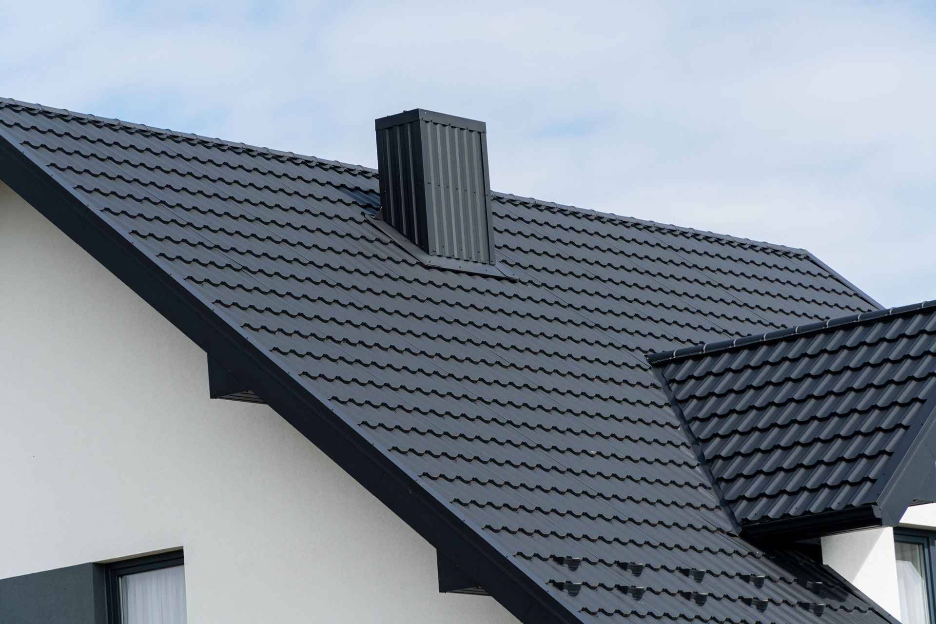 Black metal roof with matching chimney on a white house.