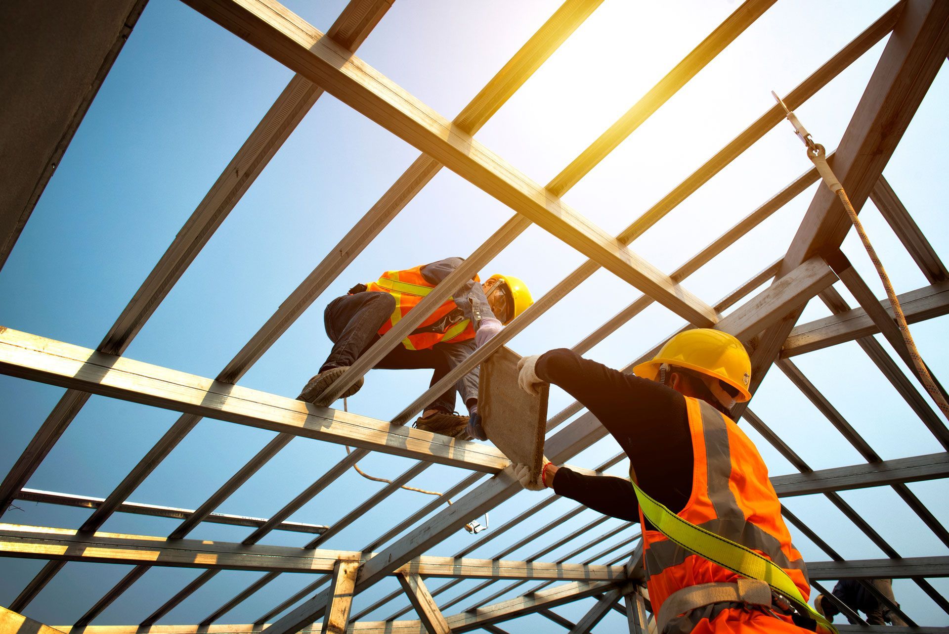 Construction workers install roof beams; wearing safety vests and hard hats under a bright sky.