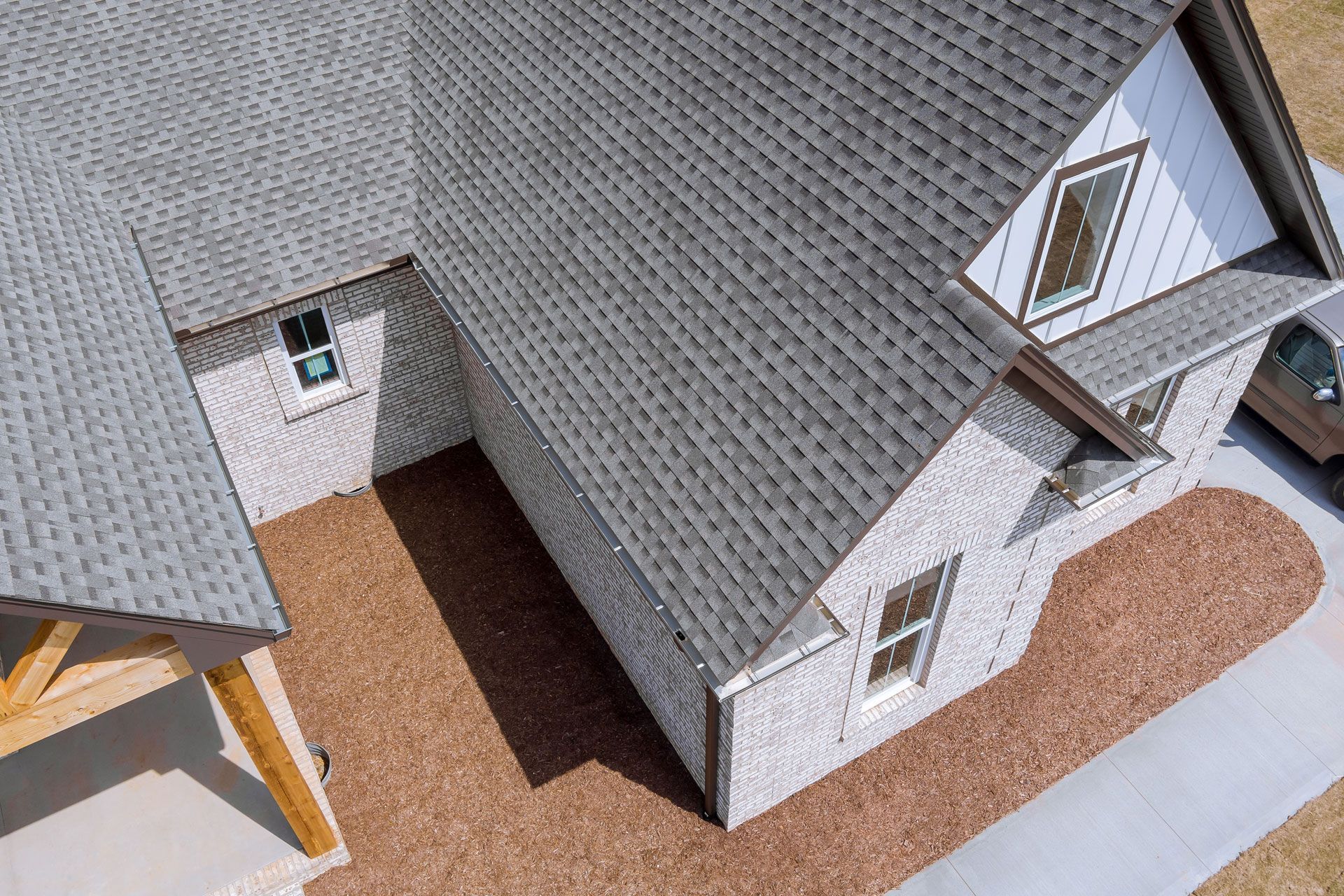 Gray roof and brick house with windows, brown yard, and concrete path.