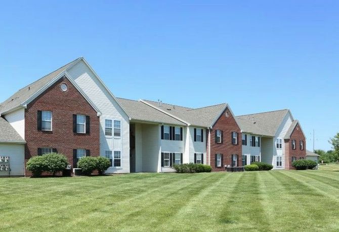 Two-story apartment building with brick and white siding, green lawn, and blue sky.