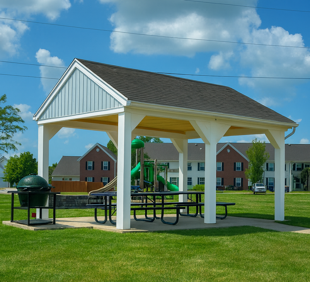 Picnic shelter in a park with a grill and playground in the background on a sunny day.