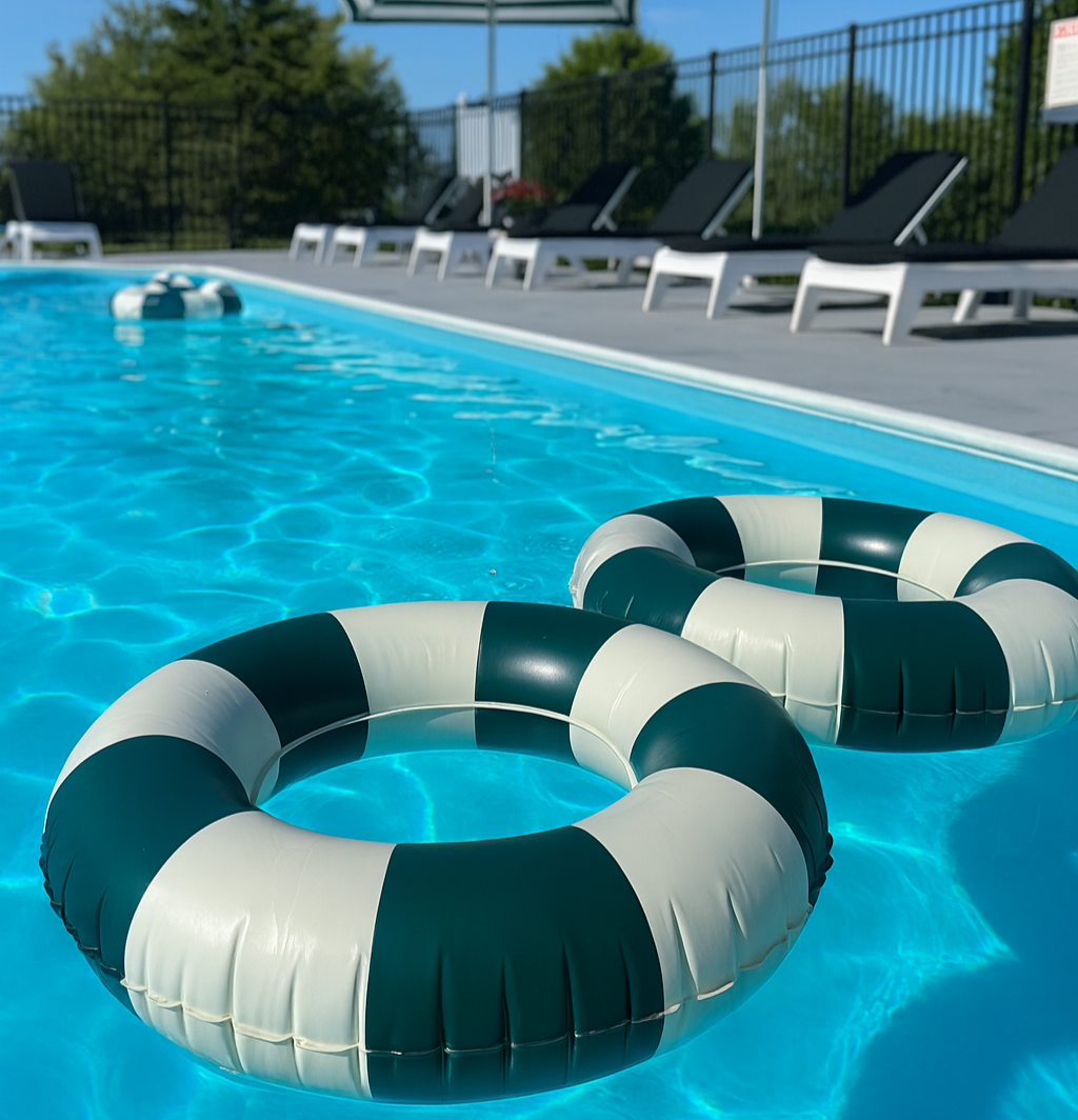 Two dark green and white striped pool floats in a pool, lounge chairs in the background.
