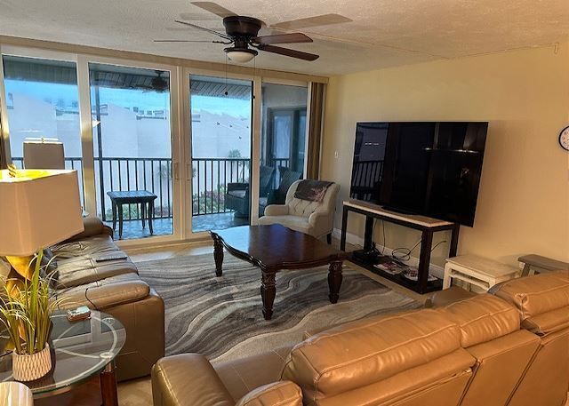 A living room with a couch , chair , table , television and ceiling fan.