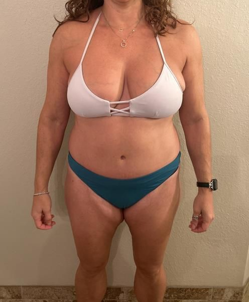 Woman in a white bikini top and teal bottoms, standing in front of a wall.