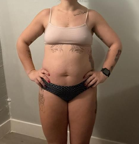 Person in a light pink sports bra and black polka dot underwear stands with hands on hips.