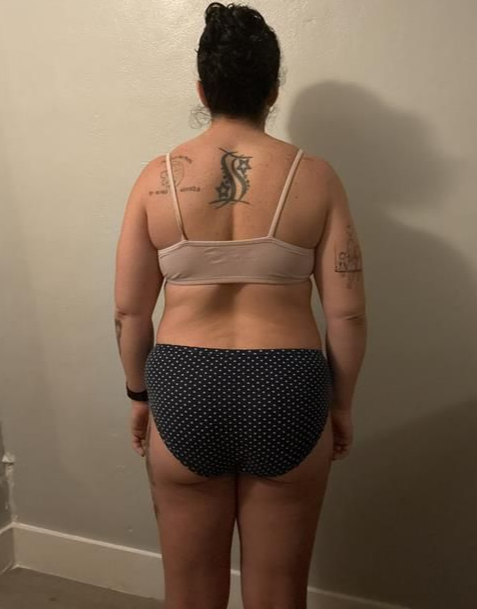 Person from the back wearing a bra and polka-dot underwear, against a neutral wall.