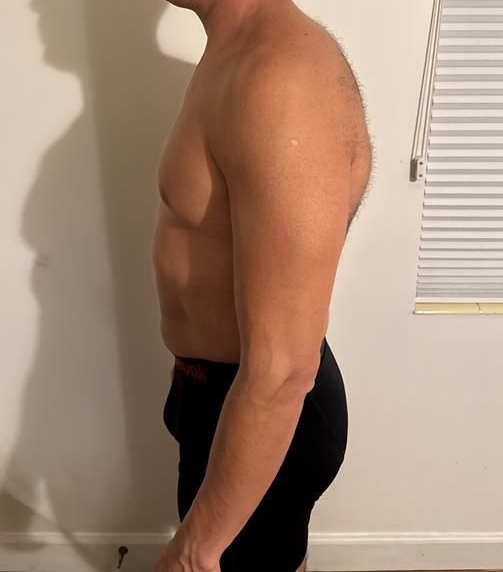 Woman in black athletic wear stands sideways near a wall.