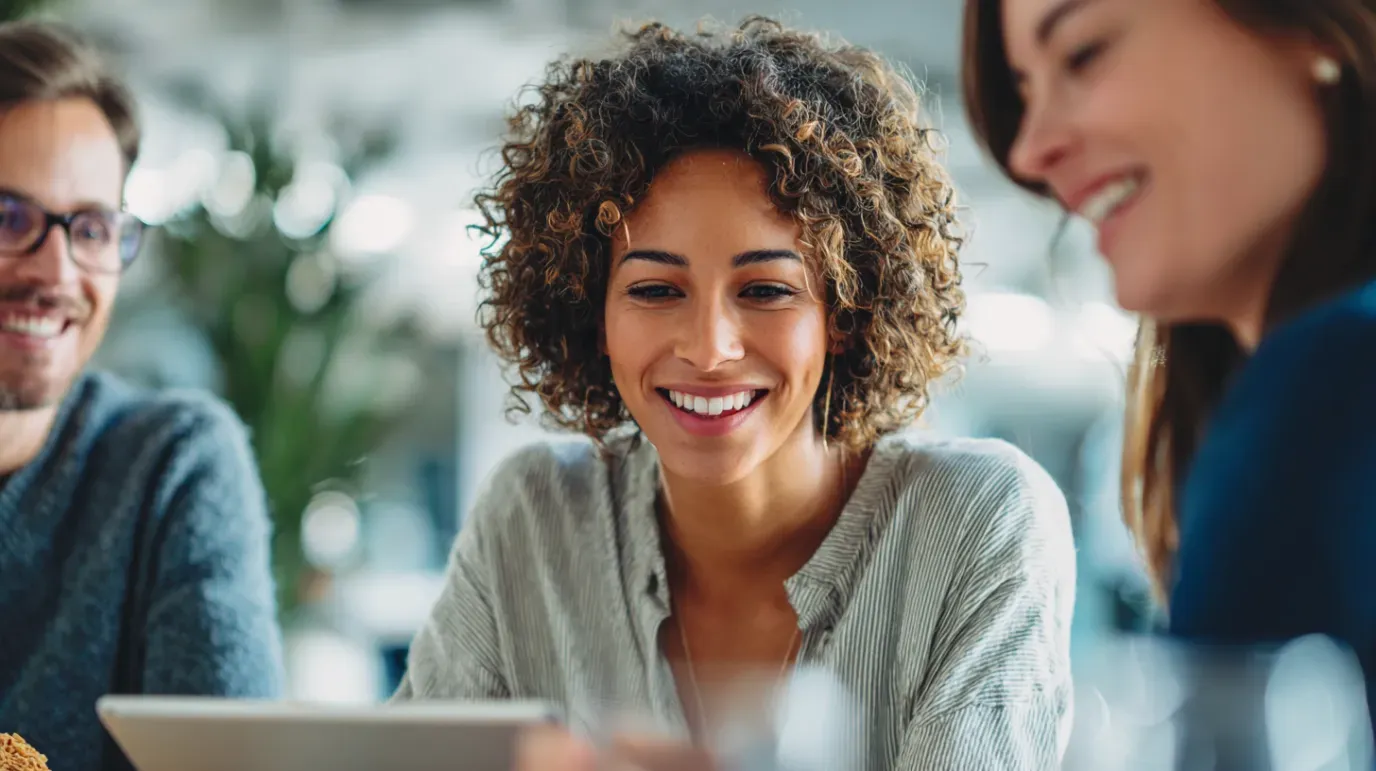 Three people smiling, looking at a tablet in a well-lit space.