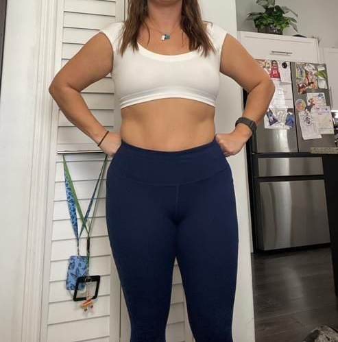 Person wearing a white crop top and blue leggings with hands on hips. Standing in a kitchen.