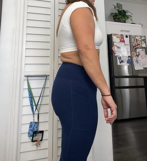 Woman in black athletic wear stands sideways near a wall.