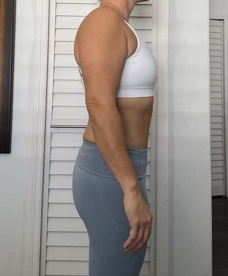 Woman in athletic wear, standing sideways, arms at her side, against a white shutter door.