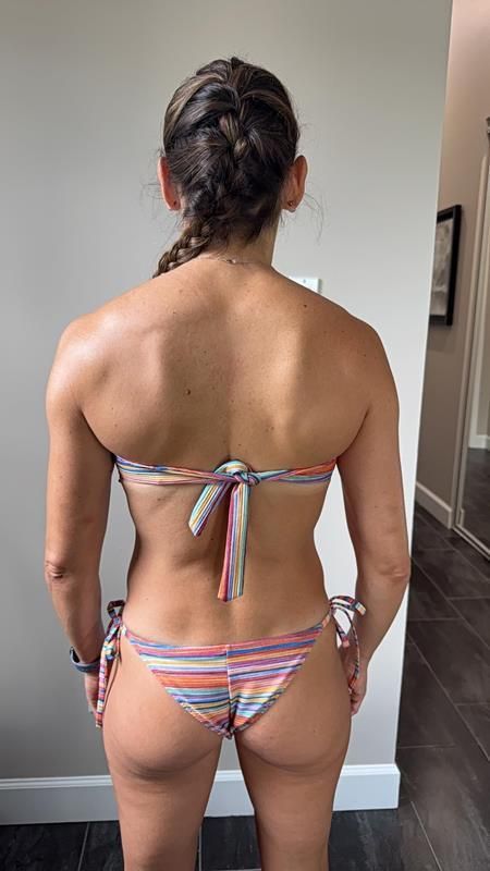 Woman in bikini, back view, standing in a hallway.  Braided hair, tan skin, striped bikini.