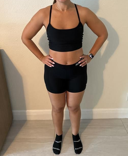 Woman in black athletic outfit stands, hands on hips, indoors.