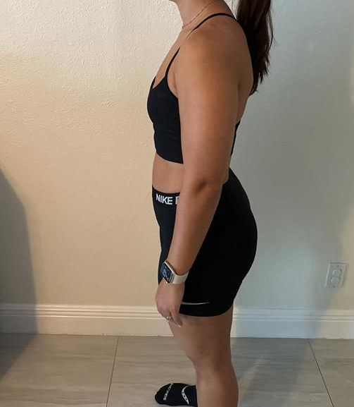 Woman in black athletic wear stands sideways near a wall.