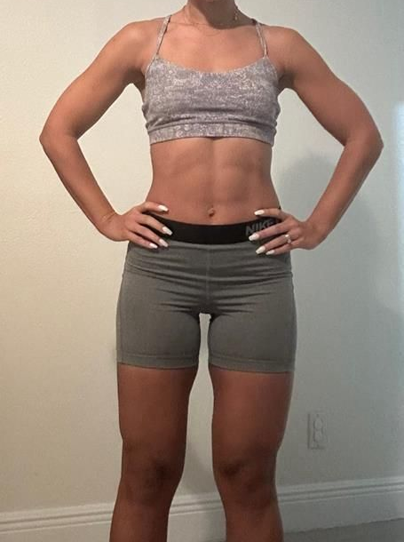 Woman in athletic wear poses with hands on hips, showcasing toned physique.