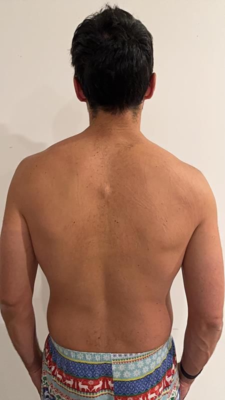 Man's back, facing away. Muscular build, dark hair. Wearing festive patterned shorts and a wrist band.