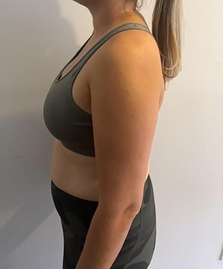 Woman in black athletic wear stands sideways near a wall.