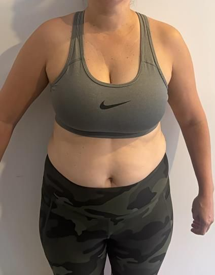 Woman in sports bra and leggings, standing with arms at sides, against a plain wall.