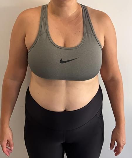 Person in a gray sports bra and black leggings, standing in front of a white wall.