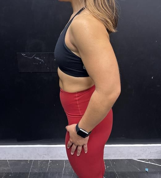 Woman in black athletic wear stands sideways near a wall.