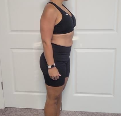 Woman in black sports bra and shorts stands, side view, against a white door.
