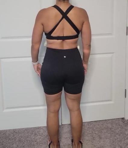 Person from the back in a black sports bra and shorts; standing indoors, wearing sandals.