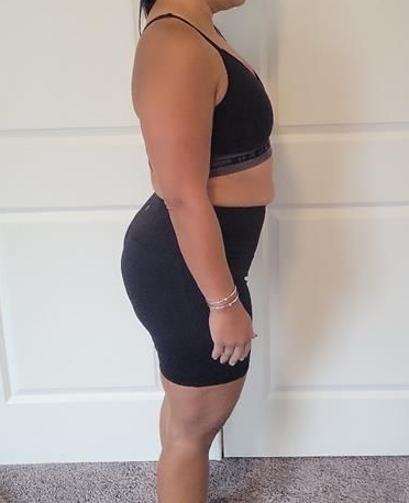 Woman in black athletic wear stands sideways near a wall.