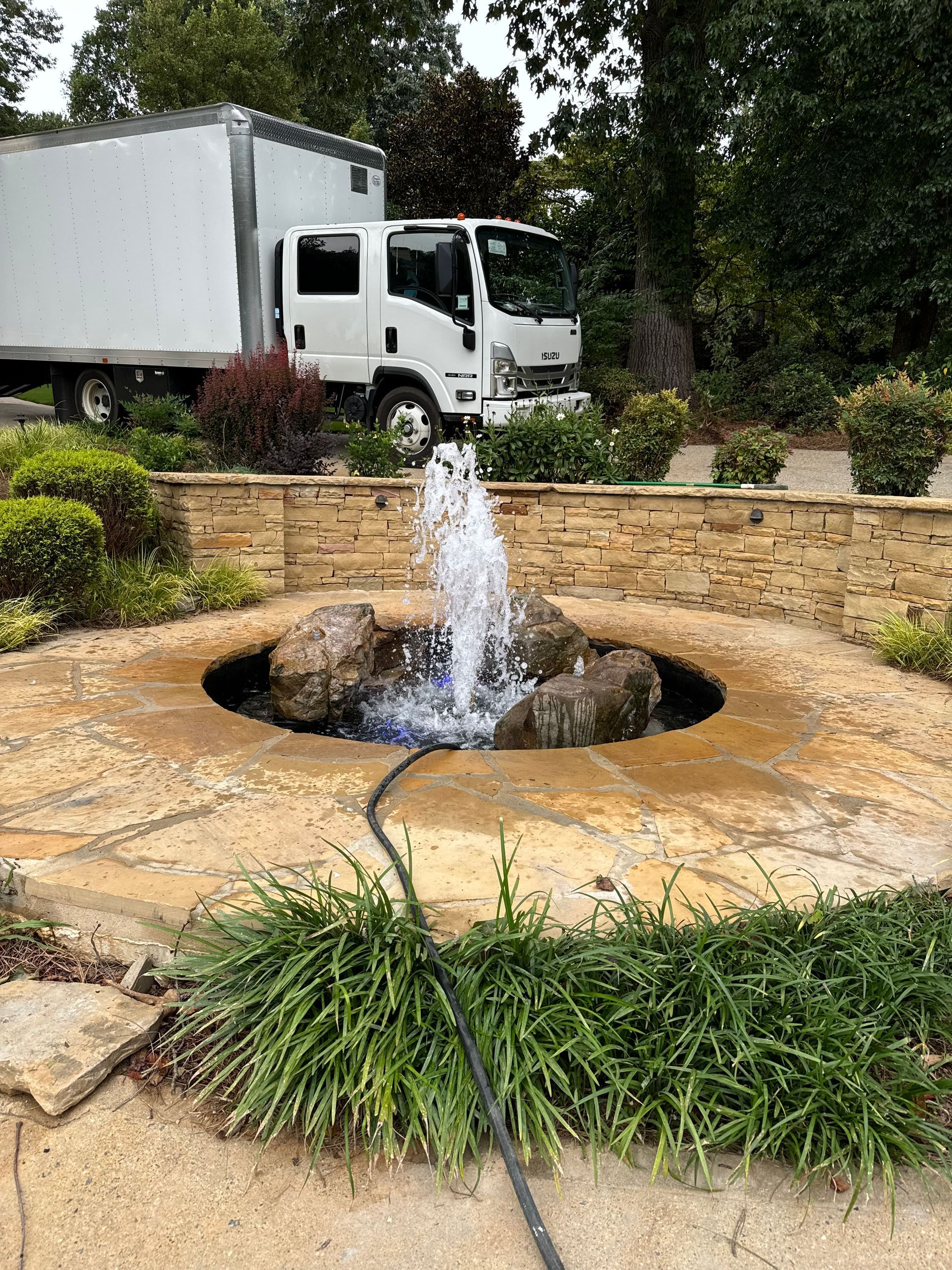 A fountain in a garden with a truck in the background.