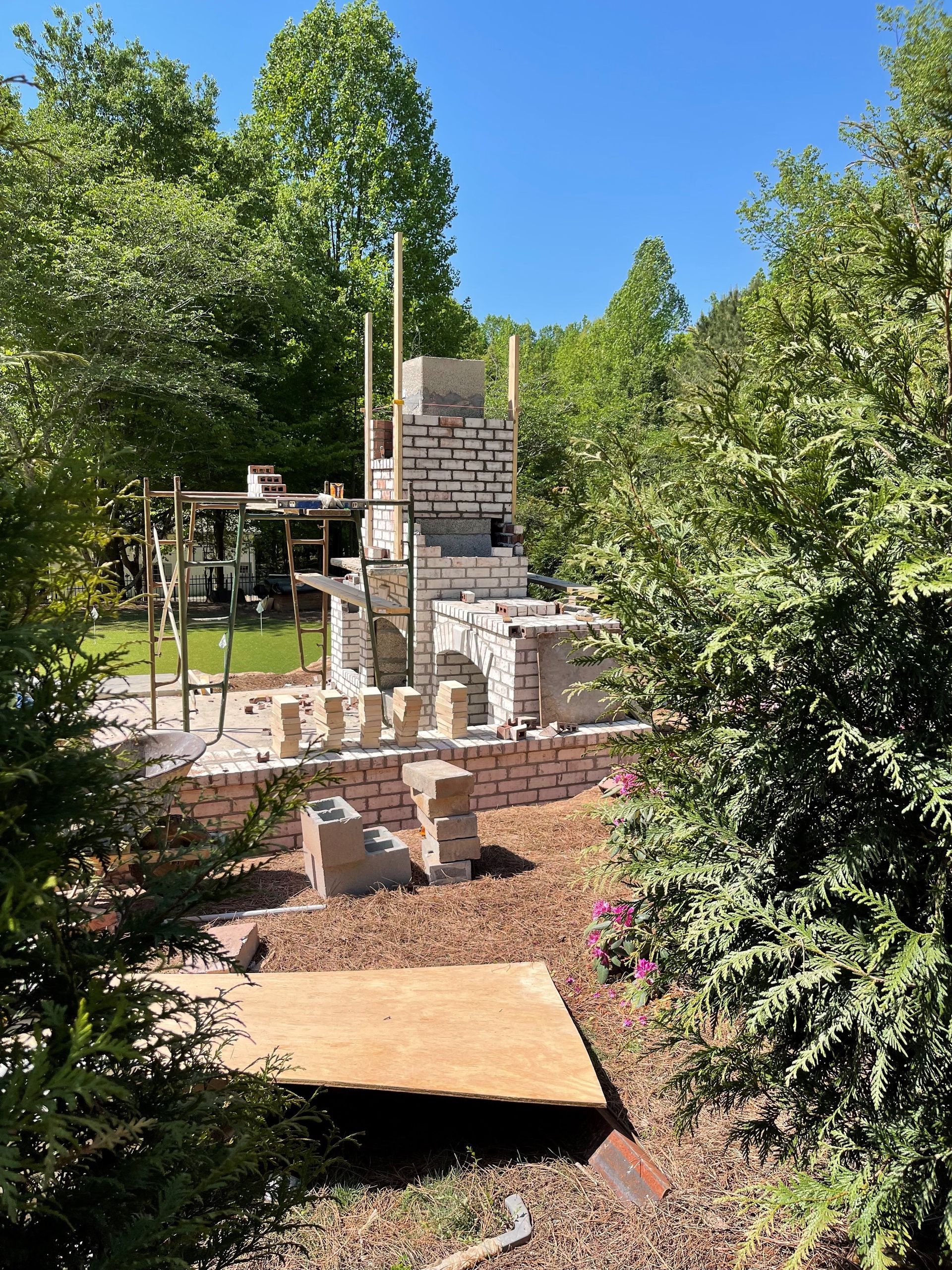 A brick fireplace is being built in a backyard surrounded by trees — Dawsonville, GA — Dixie Landscapes