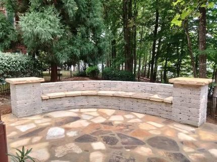 A curved brick bench is sitting on a stone patio in the middle of a forest. — Dawsonville, GA — Dixie Landscapes