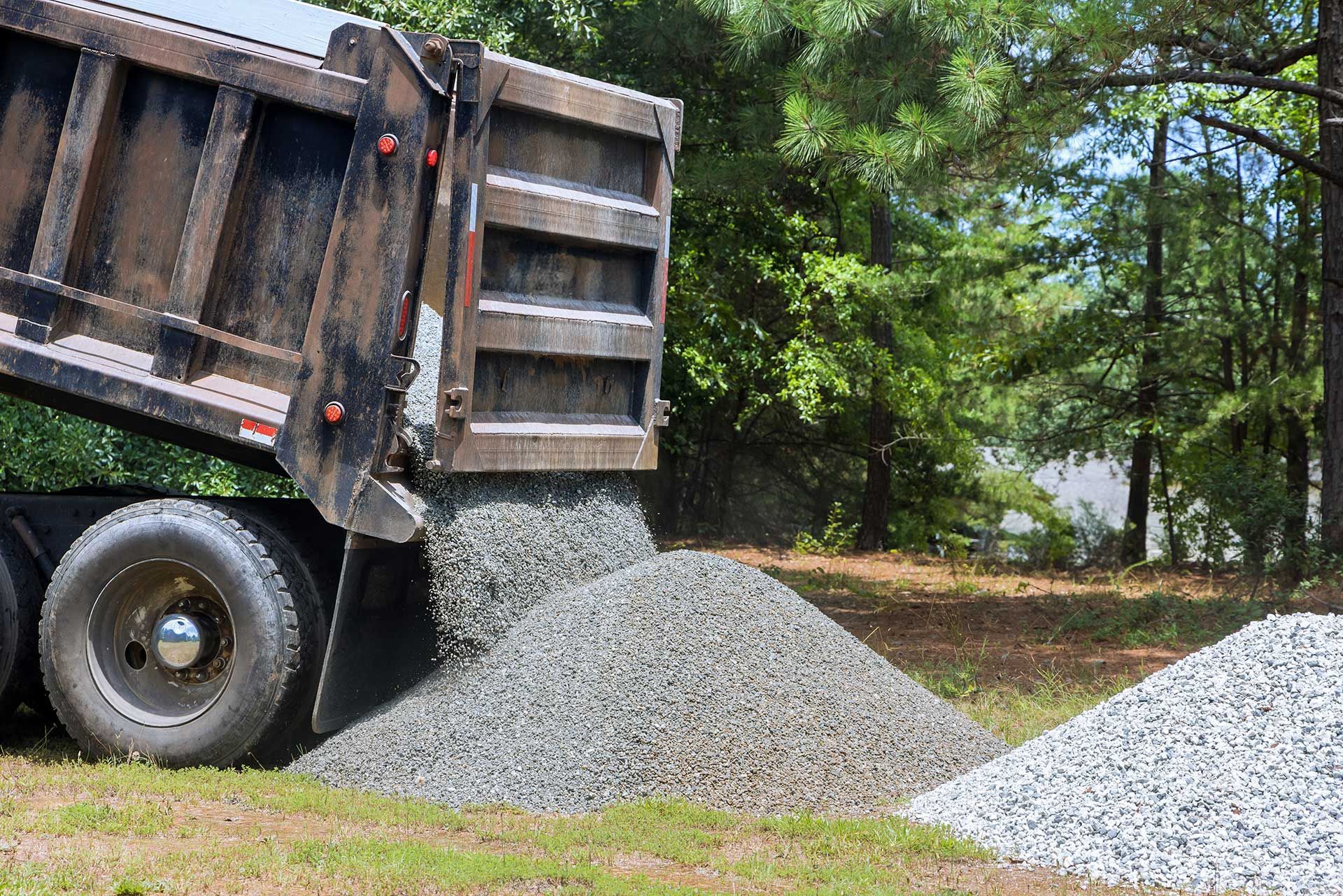 ruck unloads gravel onto grassy area preparing for landscaping work process demonstrates delivery of construction materials for improvement projects.