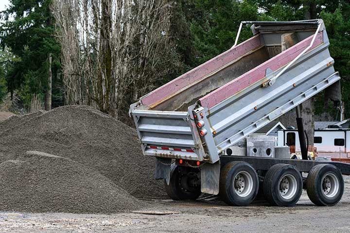 Construction dump truck unloading gravel with a hydraulic lift bed spilling material onto the ground, as a job site