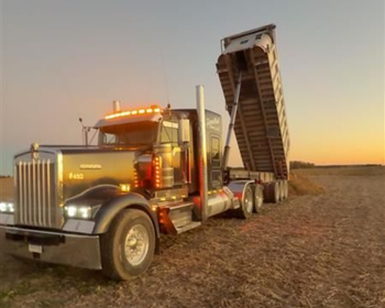 truck full of grain arriving at destination in a country road in a field of sunflower 
