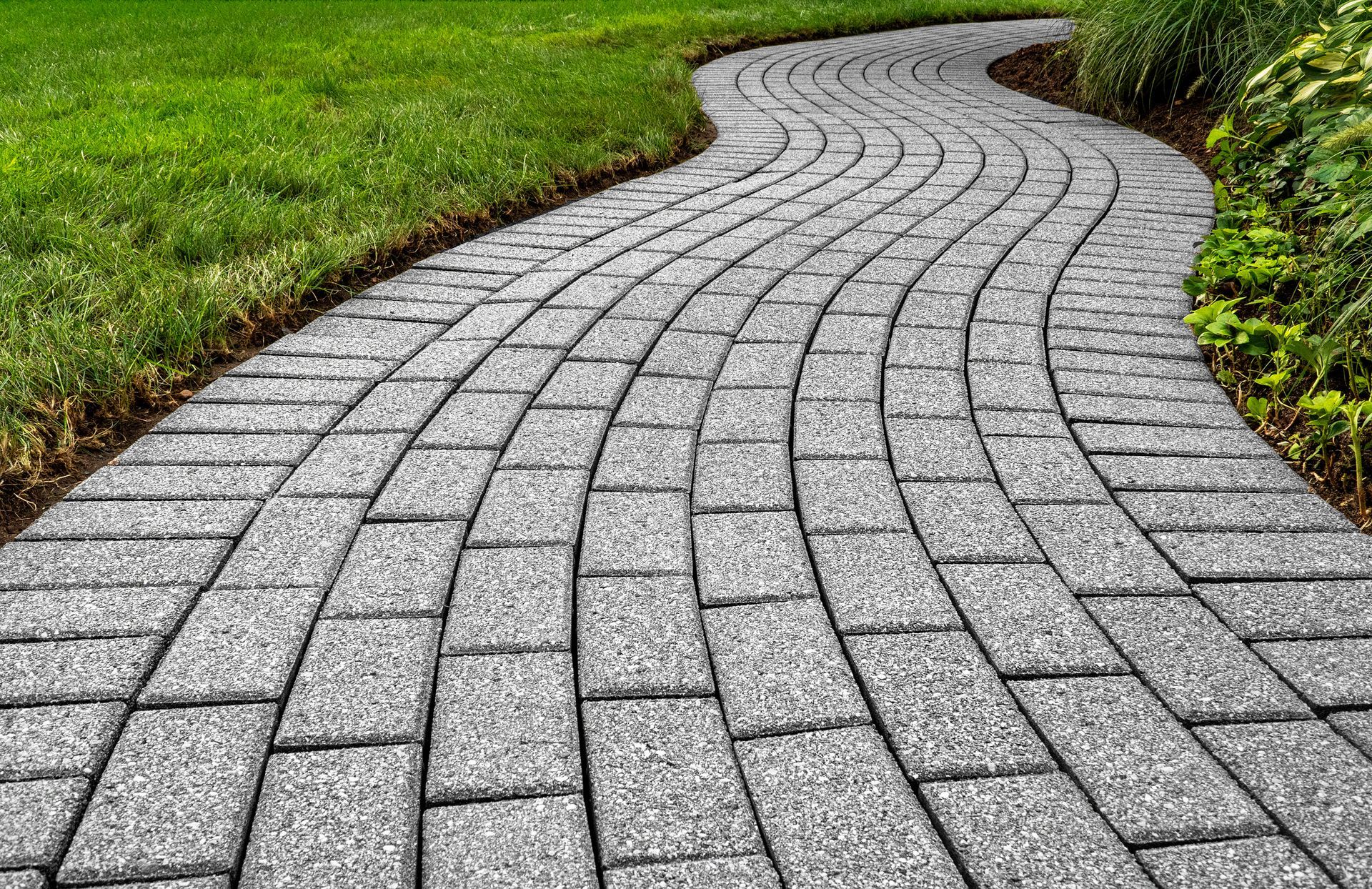 A curved brick walkway leading to a lush green lawn.