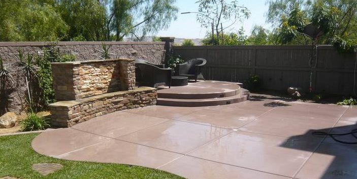 A patio with steps and a stone wall in the backyard of a house.