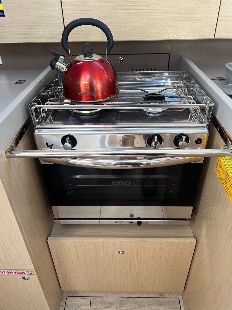 Stainless steel boat galley with stovetop, red kettle, oven, and wood cabinetry - Dunnrite Plumbing Services Cannonvale in Cannon Valley, QLD