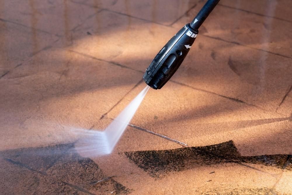 A person is using a high pressure washer to clean a tiled floor.