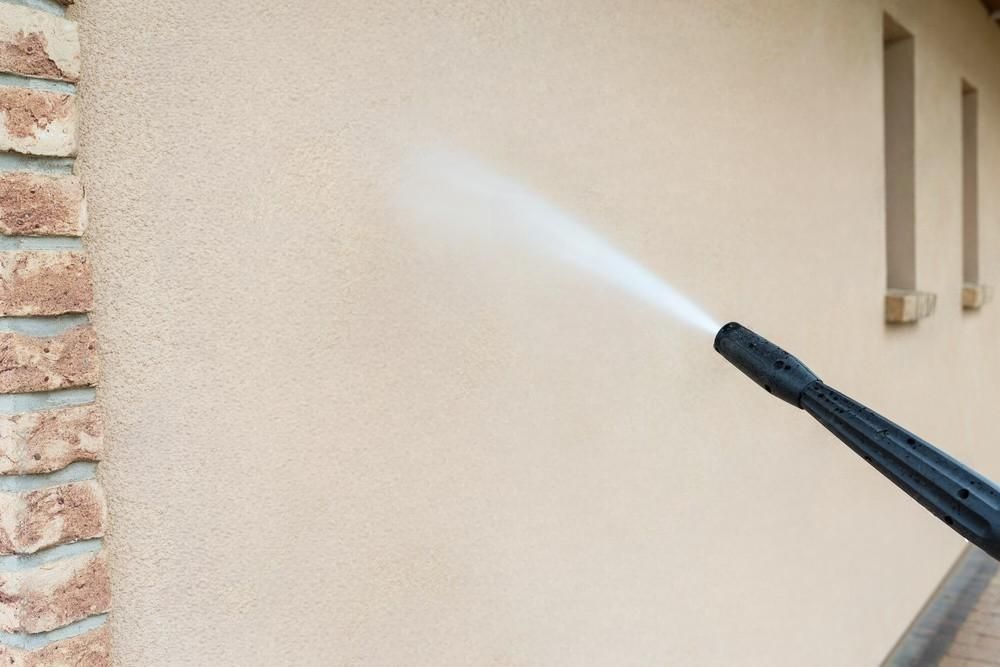 A person is using a high pressure washer to clean the side of a building.