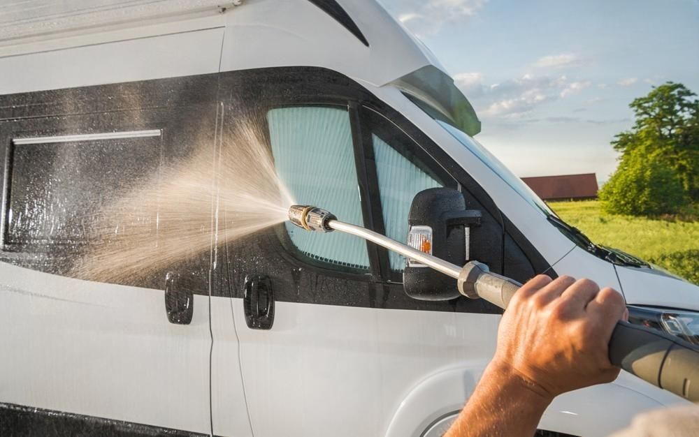 A person is washing a camper van with a high pressure washer.