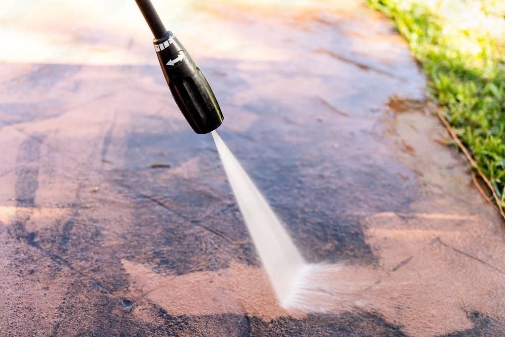 A person is using a high pressure washer to clean a sidewalk.