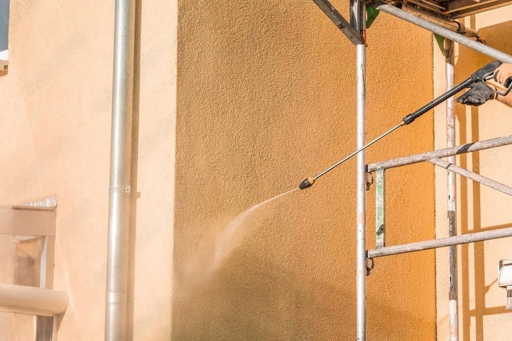 A man is cleaning the side of a building with a high pressure washer.