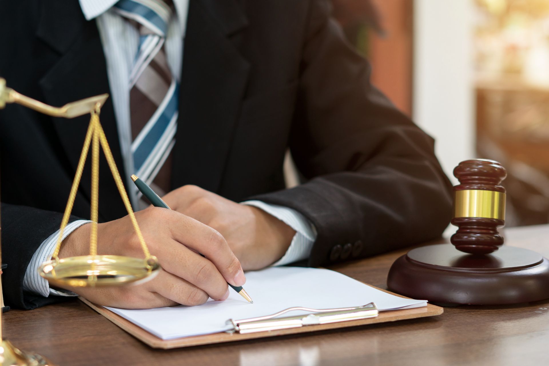 Lawyer writing notes beside scales of justice and courtroom gavel.