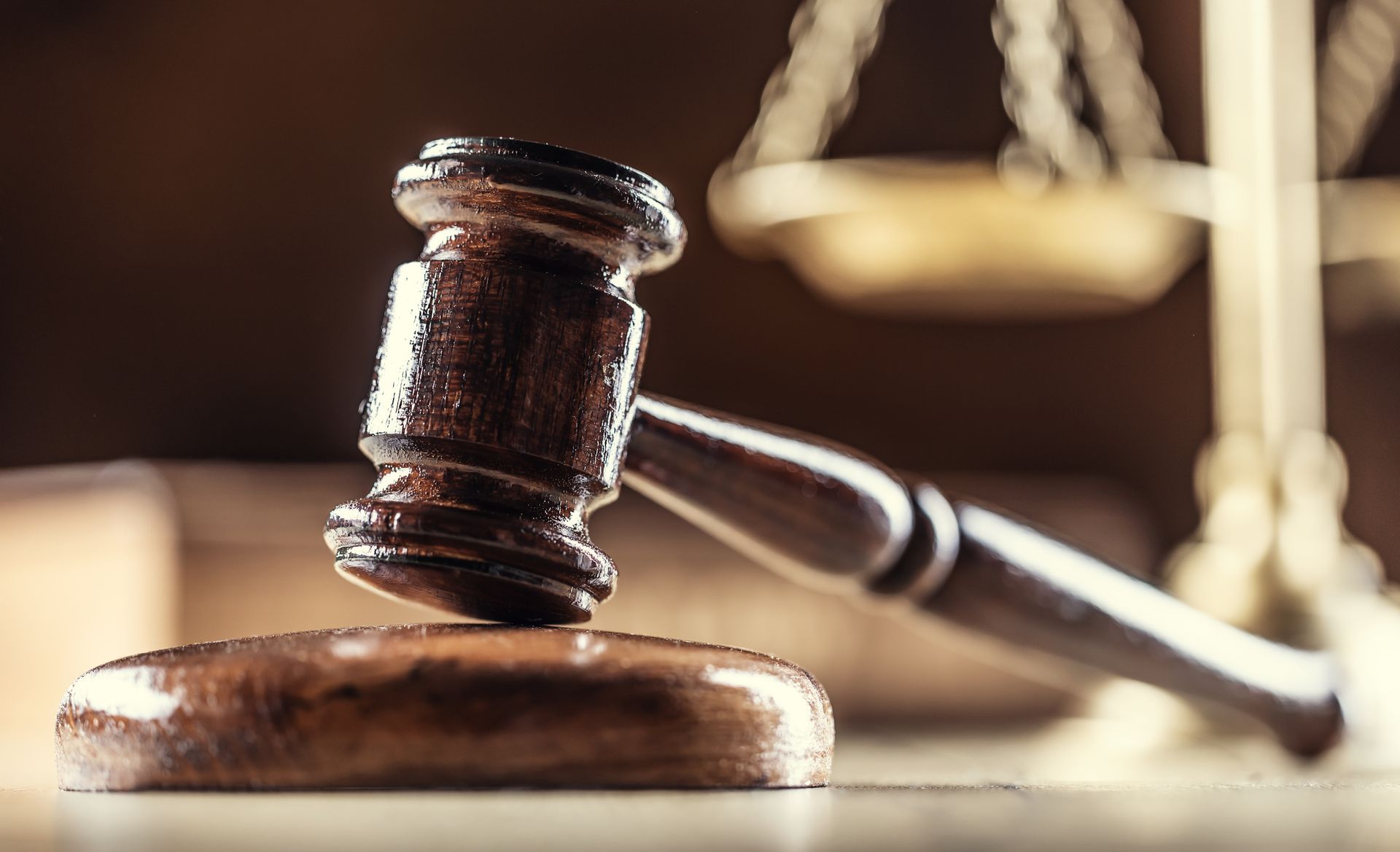 Close-up of a wooden judge’s gavel resting on a block with scales of justice in the background.