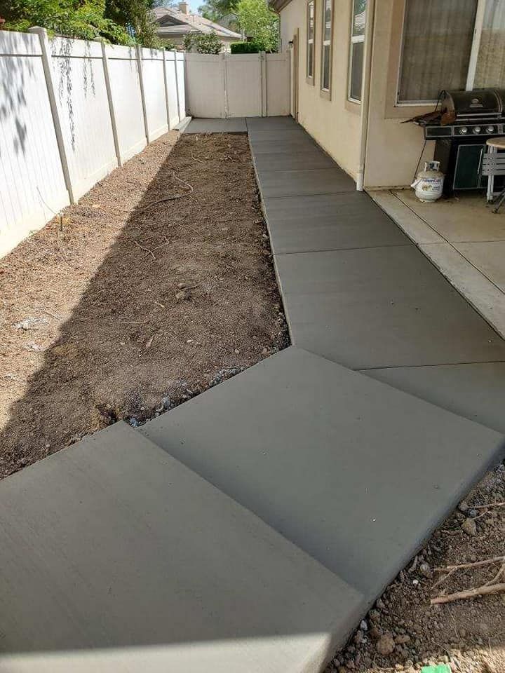 A concrete walkway is being built in the backyard of a house.