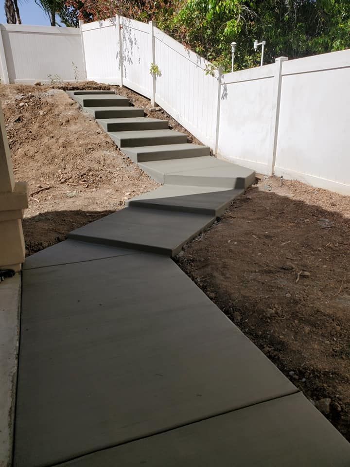 A concrete walkway with stairs leading up to a white fence.