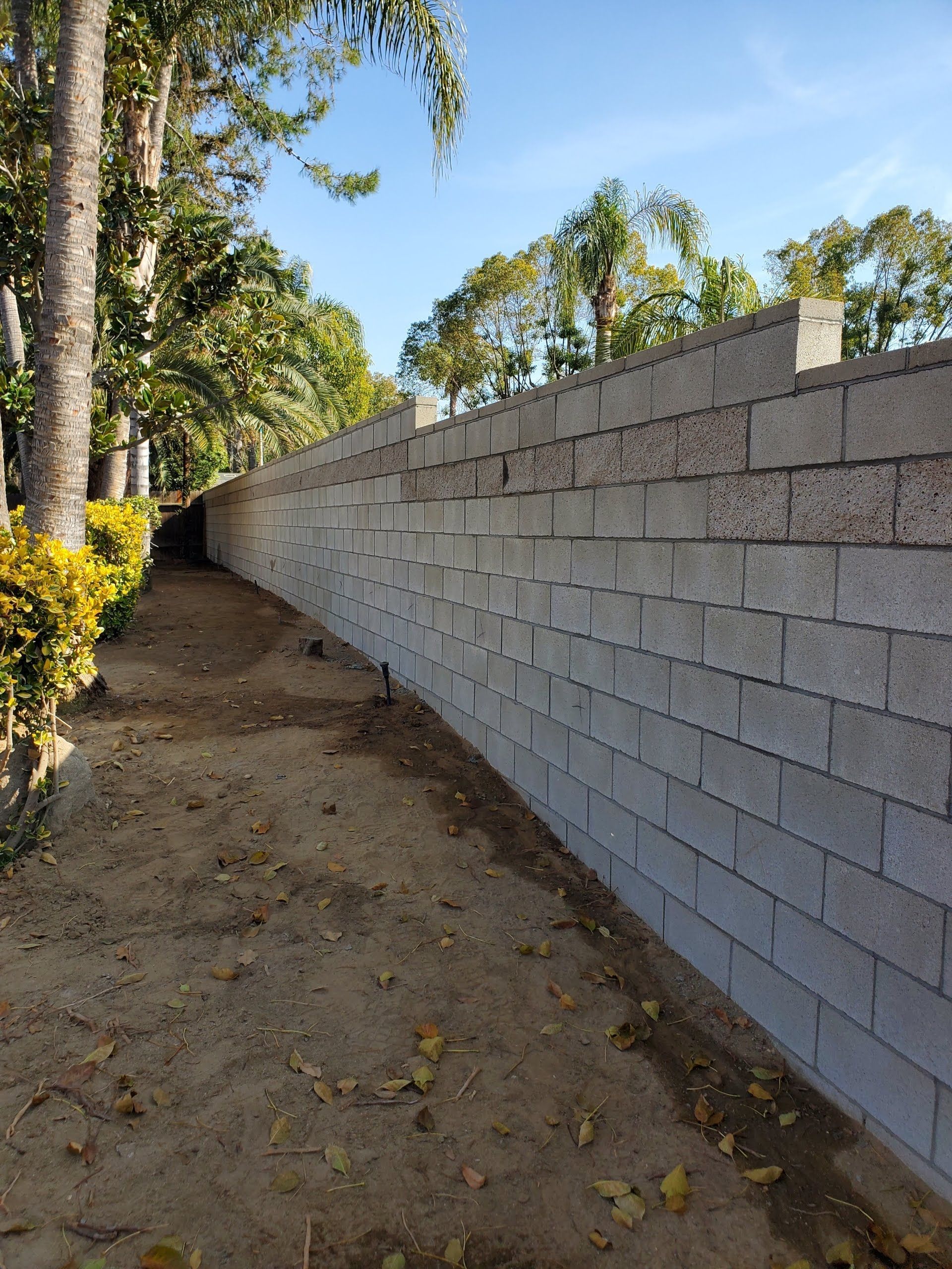 A brick wall along a dirt path with trees in the background.