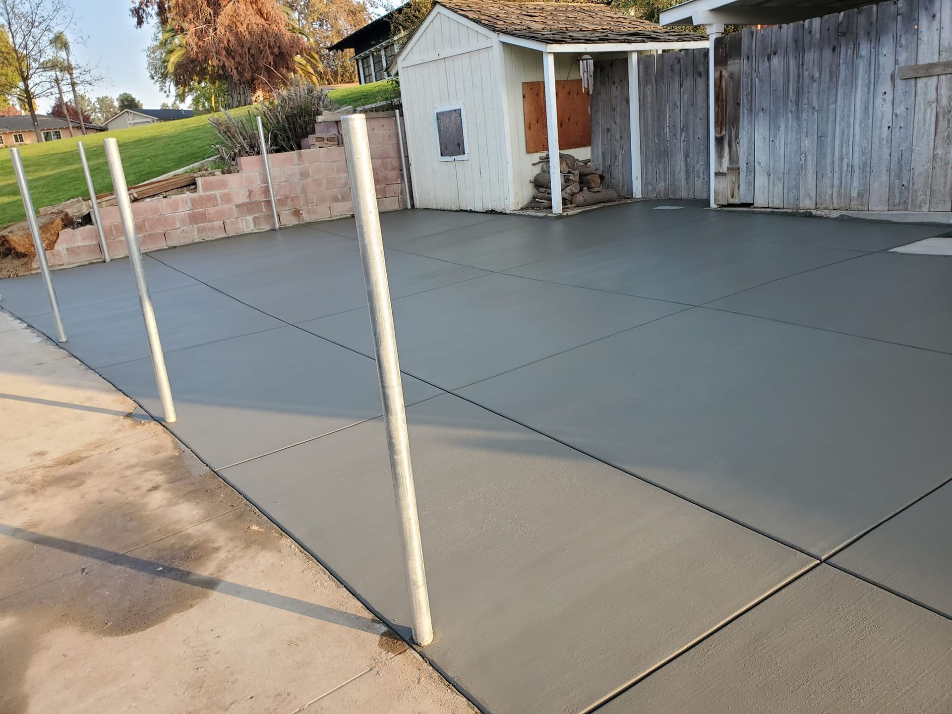 A concrete driveway with a fence and a shed in the background.