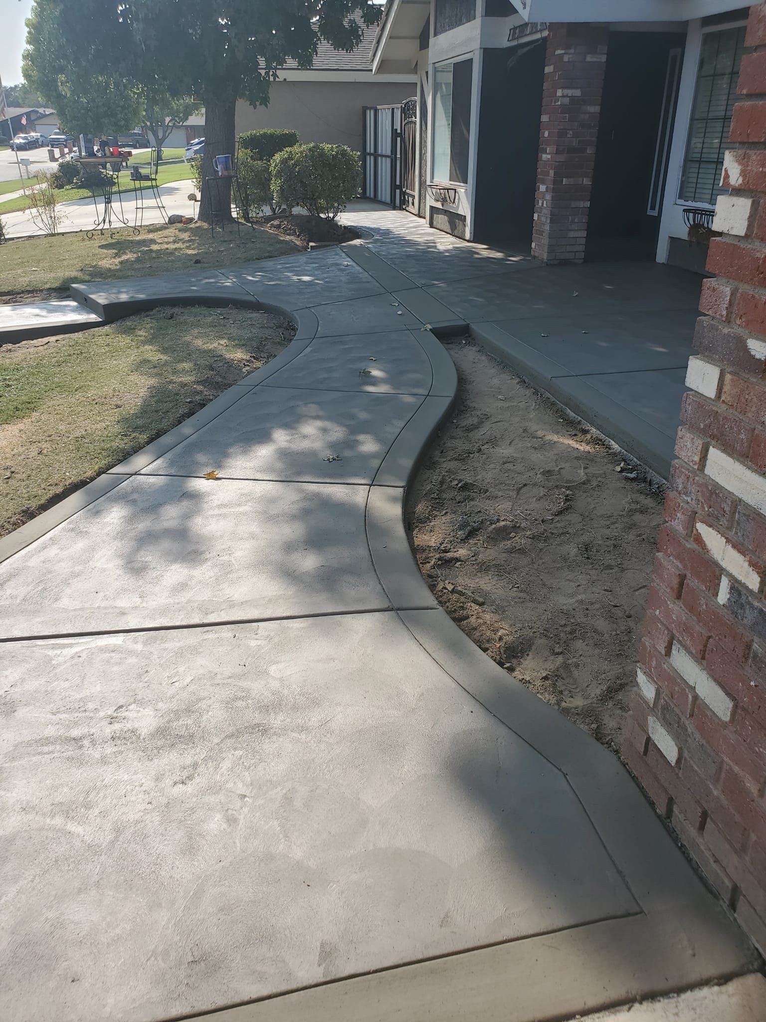 A concrete walkway leading to a house with a brick wall.