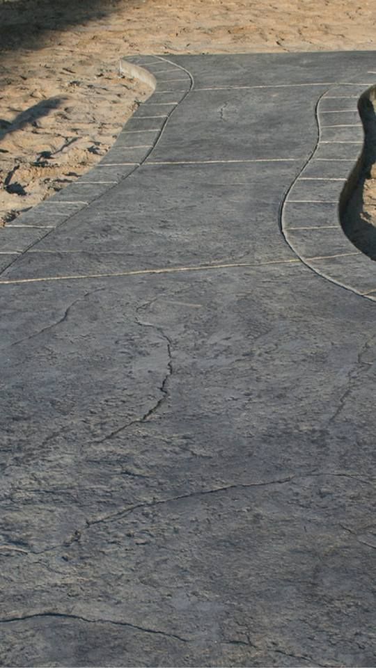 A person is walking down a concrete walkway next to a sandy area.